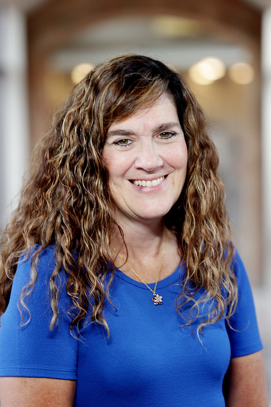 Image of a white woman with brown curly hair wearing a blue shirt.